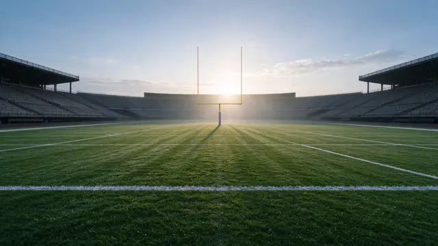 Empty American football stadium with goalposts as sunlight filters through morning haze over the grass field