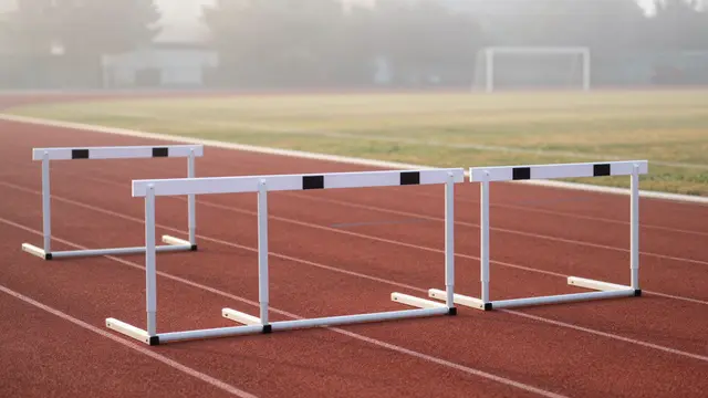 White track hurdles sit on a red running track in soft early morning fog
