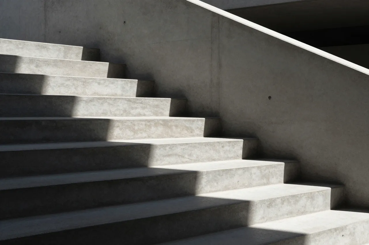 A minimalist modern concrete staircase with sharp dramatic sunlight shadows across its steps
