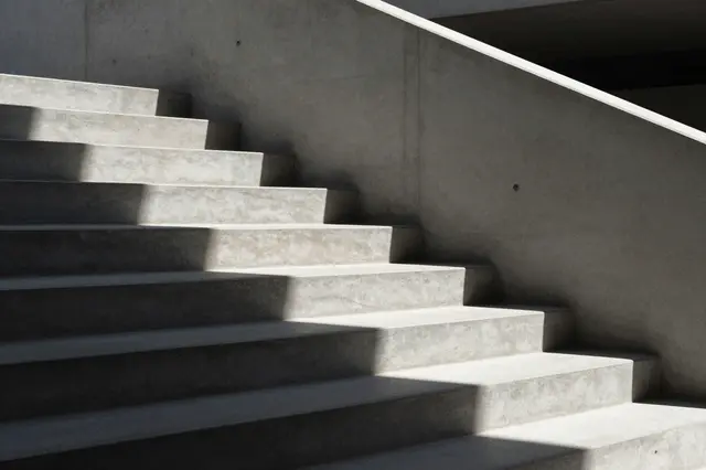 A minimalist modern concrete staircase with sharp dramatic sunlight shadows across its steps