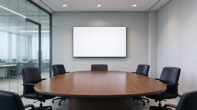Empty boardroom with oval walnut table, black leather chairs, blank display screen and glass office walls
