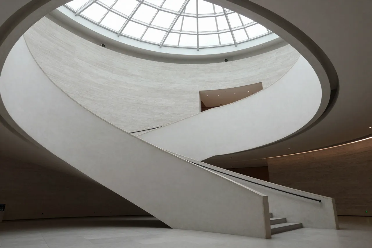 Curved concrete museum atrium with a glass domed skylight overhead