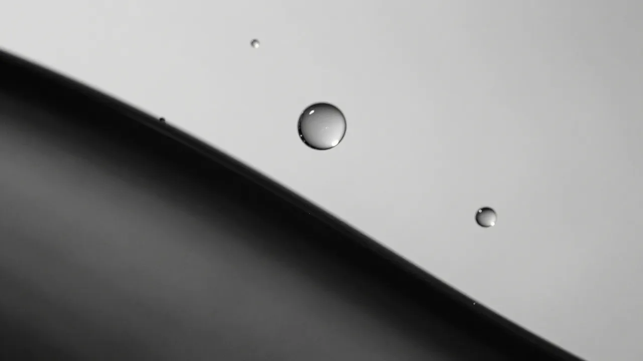 Glossy silvery water droplets rest on a slanted surface in black and white macro view