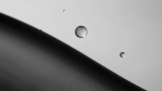 Glossy silvery water droplets rest on a slanted surface in black and white macro view