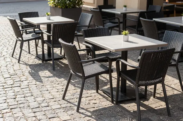 Empty outdoor cafe tables with small succulents sit on a sunlit cobblestone square at morning