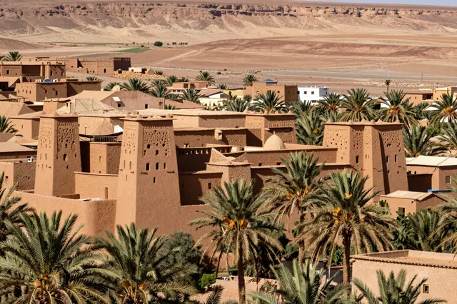Earthen kasbah buildings sit among palm trees in a sunbaked desert valley