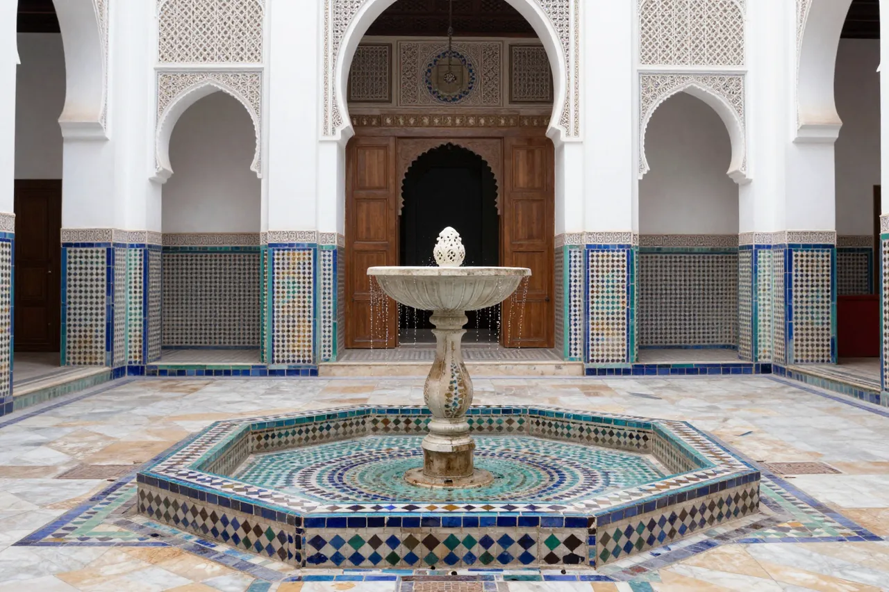Ornate zellij tile fountain sits at the center of a traditional white Moroccan riad courtyard with carved arches