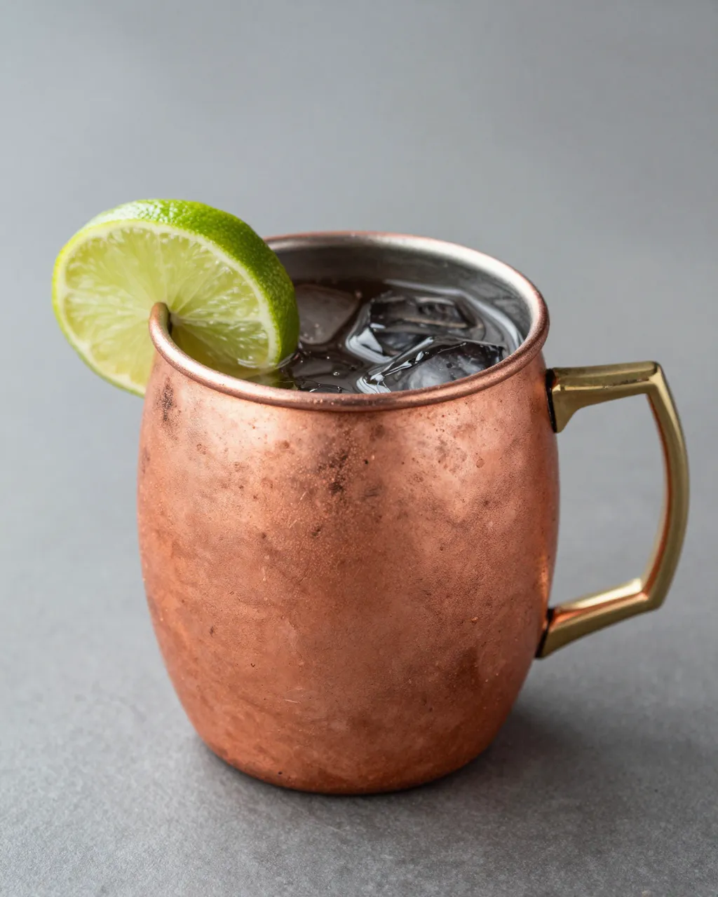 A copper Moscow mule mug with ice and a lime slice sits on a gray neutral background