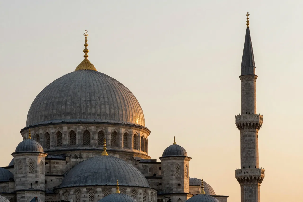 Ornate stone mosque domes and a tall minaret stand against a soft warm sunset sky.