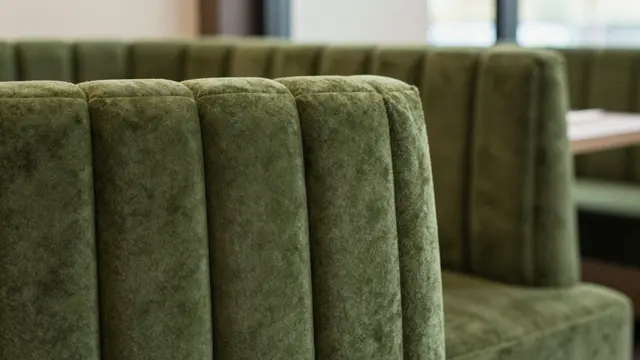Close-up of a tufted moss-green velvet restaurant banquette with a softly blurred background