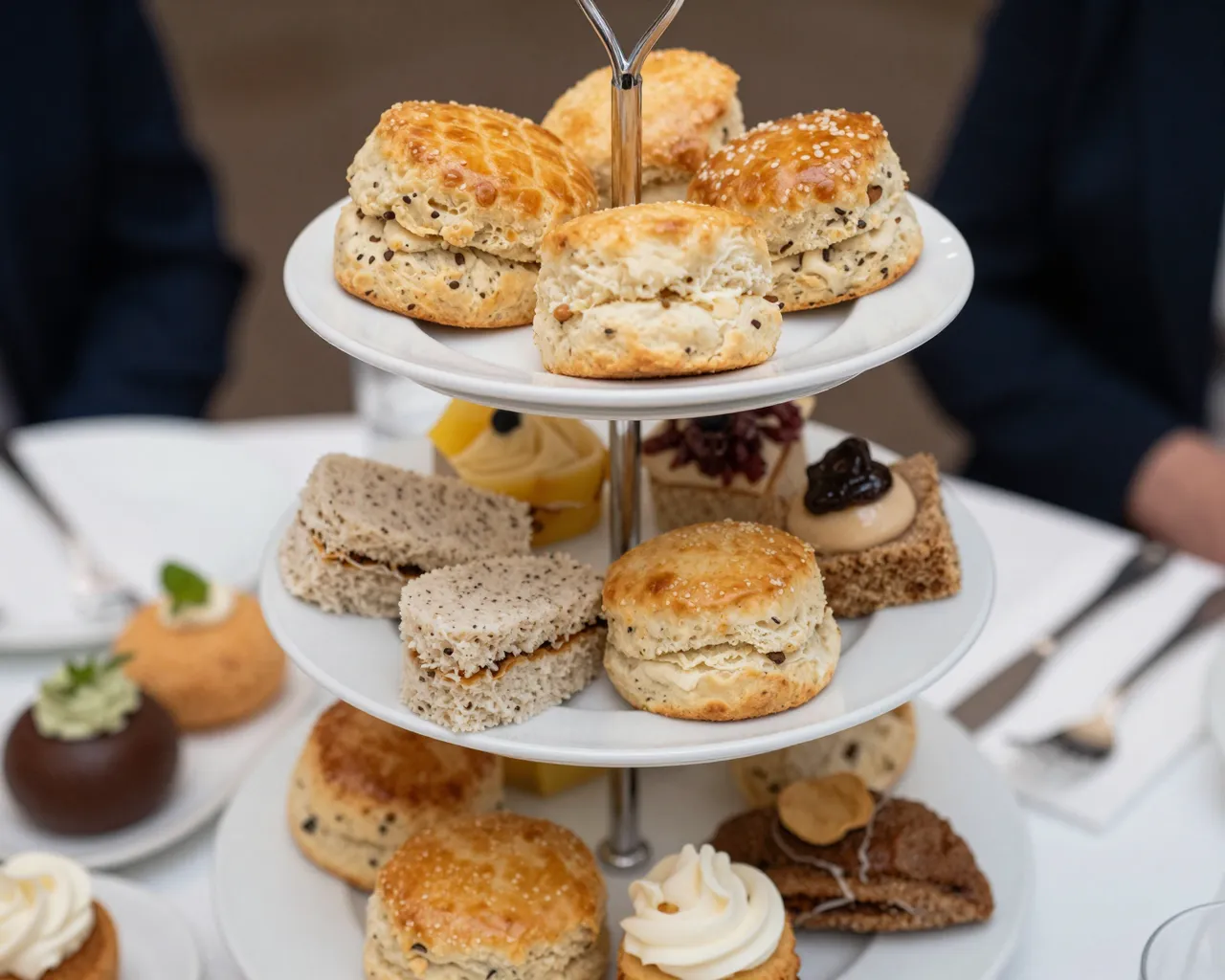 Three tiered ceramic stand filled with scones, finger sandwiches and pastries set on a white tablecloth table