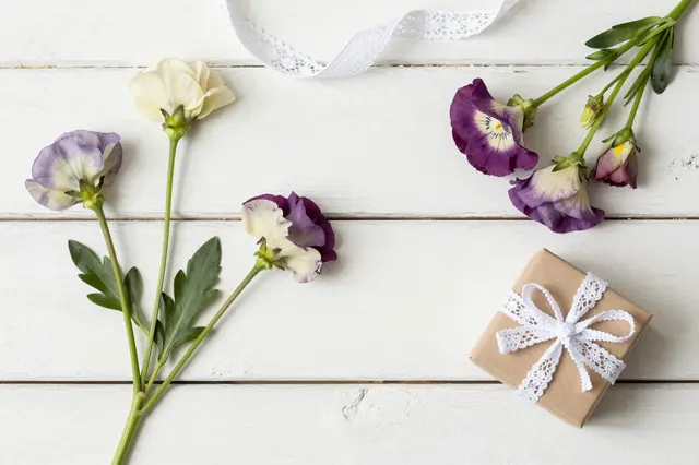 Pansy flowers, lace ribbon and a small gift box arranged on weathered white wooden planks