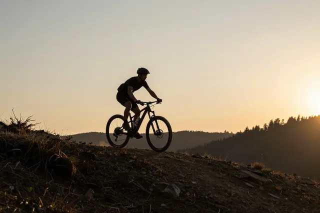 Silhouetted mountain biker rides along a rocky forest ridge at golden sunset