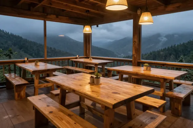 Empty wooden mountain hut dining area lit by warm pendant lamps overlooking stormy forested mountains
