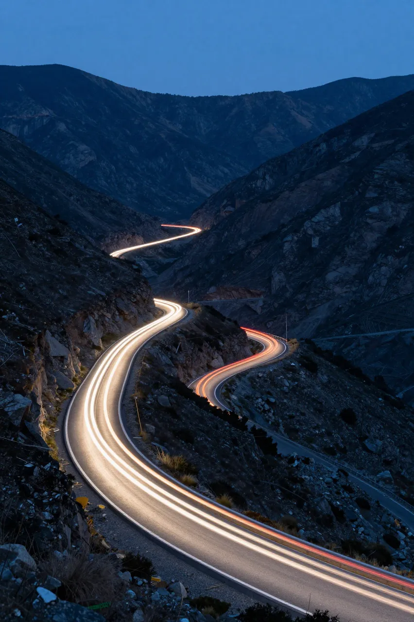 Long exposure light trails from moving vehicles wind along a winding mountain pass at blue hour