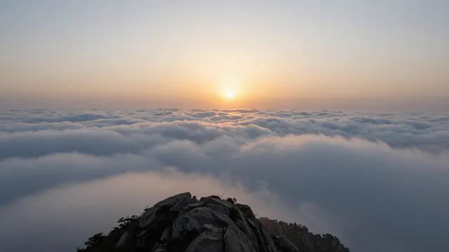 Bright sunrise glows above a vast sea of clouds viewed from a rocky mountain peak