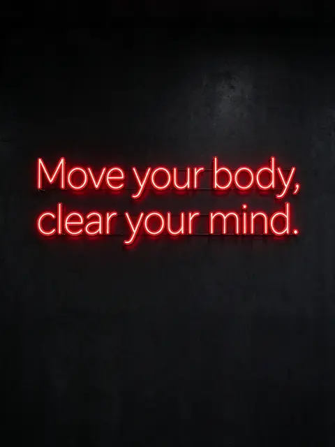Glowing red neon sign reading "Move your body, clear your mind." mounted on a dark textured wall