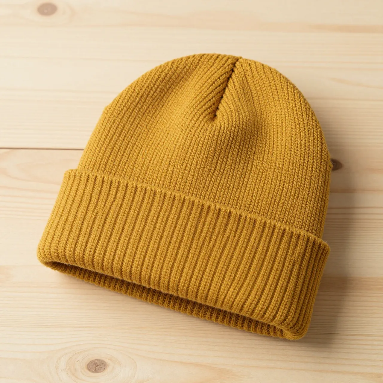 A folded cuff mustard yellow knit beanie rests flat on a light pine wooden surface