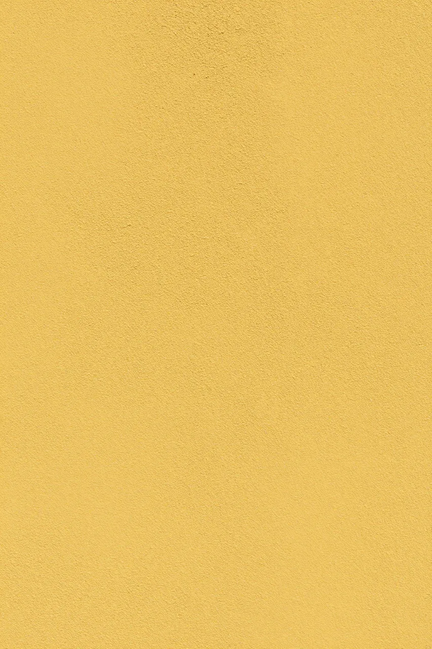 Full frame close-up of coarse dabbed mustard yellow stucco under even flat lighting