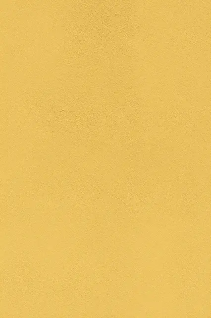 Full frame close-up of coarse dabbed mustard yellow stucco under even flat lighting