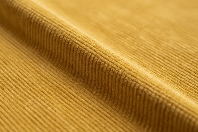 Close-up of folded mustard yellow corduroy fabric showing its soft raised ribbed surface