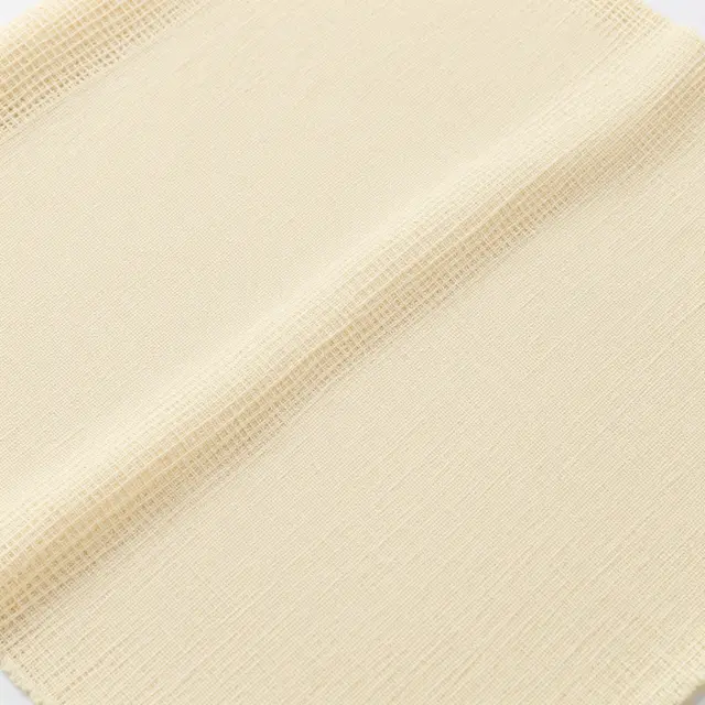 Full frame close-up of loosely woven pale beige cheesecloth fabric with a soft diagonal fold