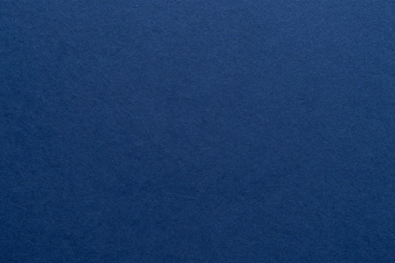 Full frame close-up of textured navy blue handmade paper under flat even lighting