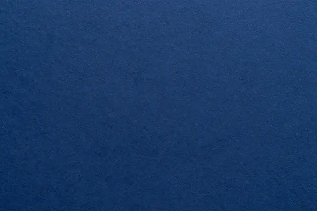 Full frame close-up of textured navy blue handmade paper under flat even lighting