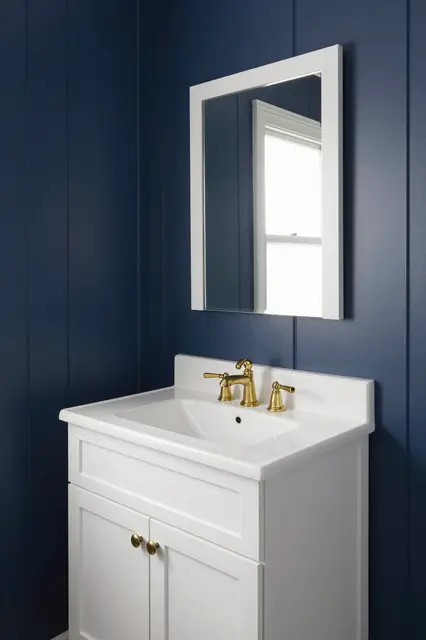 White bathroom vanity with brass hardware and framed mirror against navy board and batten walls