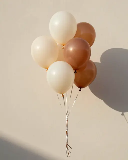 Bouquet of cream and terracotta balloons floats against a smooth plaster wall in warm afternoon light