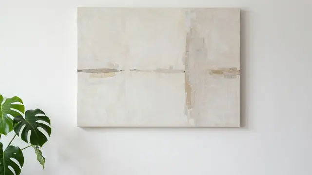 A large muted abstract canvas hangs on a plain white wall next to a potted monstera plant.