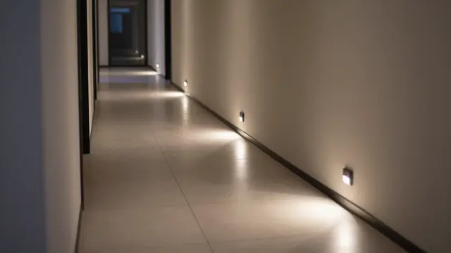 A long empty modern hallway lit by soft glowing motion-sensor floor lights after dark