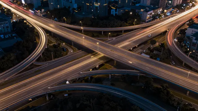 Aerial long exposure view of an illuminated multi-level highway interchange with glowing vehicle light trails at night