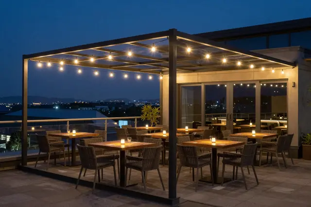 Lit rooftop restaurant terrace with string lights overlooking a city at twilight