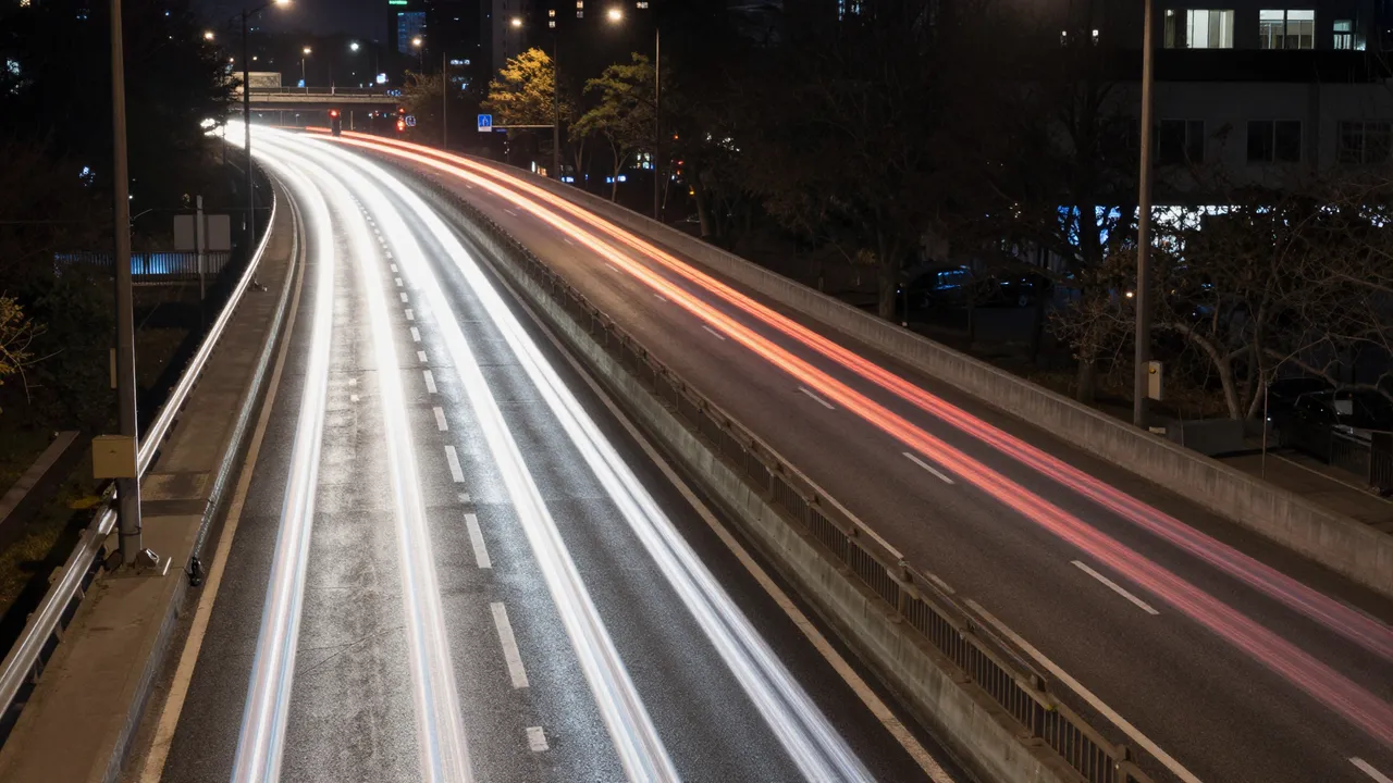 Long exposure view of bright white and red traffic light trails curving along an elevated city highway at night
