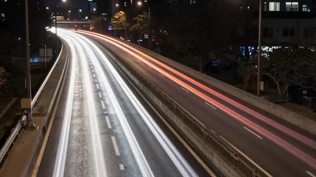 Long exposure view of bright white and red traffic light trails curving along an elevated city highway at night