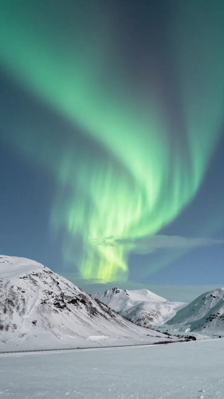 Swirling green northern lights arc across the sky above a snow-covered mountain range and frozen plain