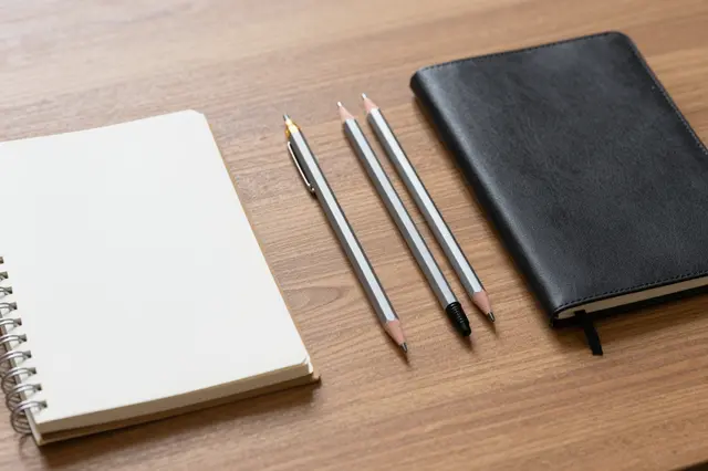 Two notebooks and three writing utensils rest neatly on a warm wood grain desk.