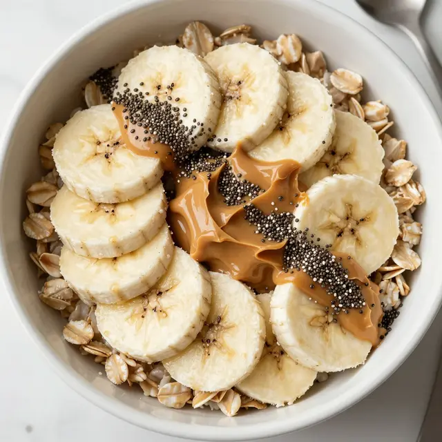 Top down view of a ceramic bowl of oatmeal topped with sliced banana, peanut butter and chia seeds on a light countertop