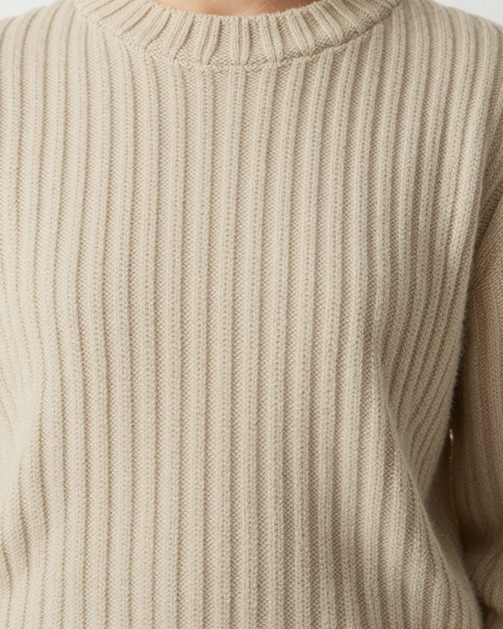 Close-up view of an oatmeal-colored ribbed knit sweater with a crew neckline