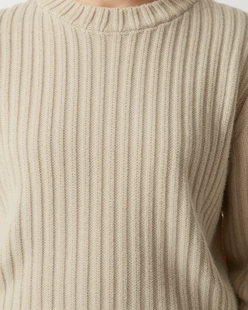 Close-up view of an oatmeal-colored ribbed knit sweater with a crew neckline