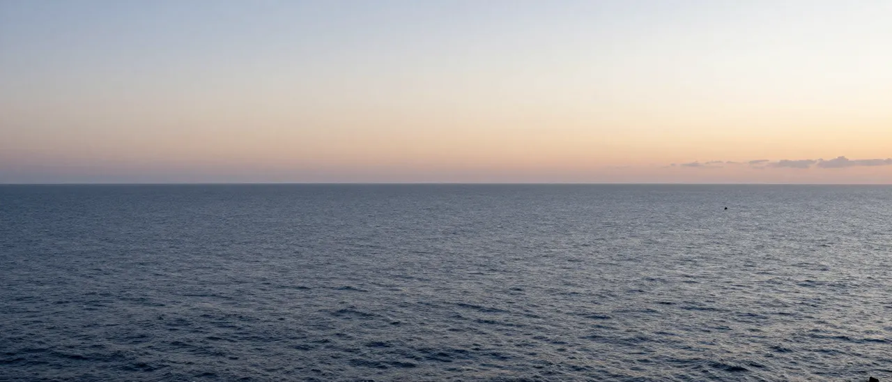 A wide calm ocean stretches out beneath a soft gradient sky at dawn