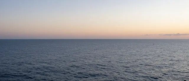 A wide calm ocean stretches out beneath a soft gradient sky at dawn