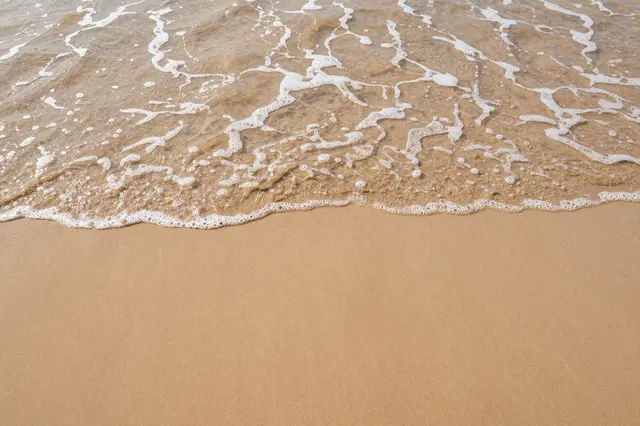 Top-down view of a foamy shallow ocean wave sliding over smooth tan beach sand