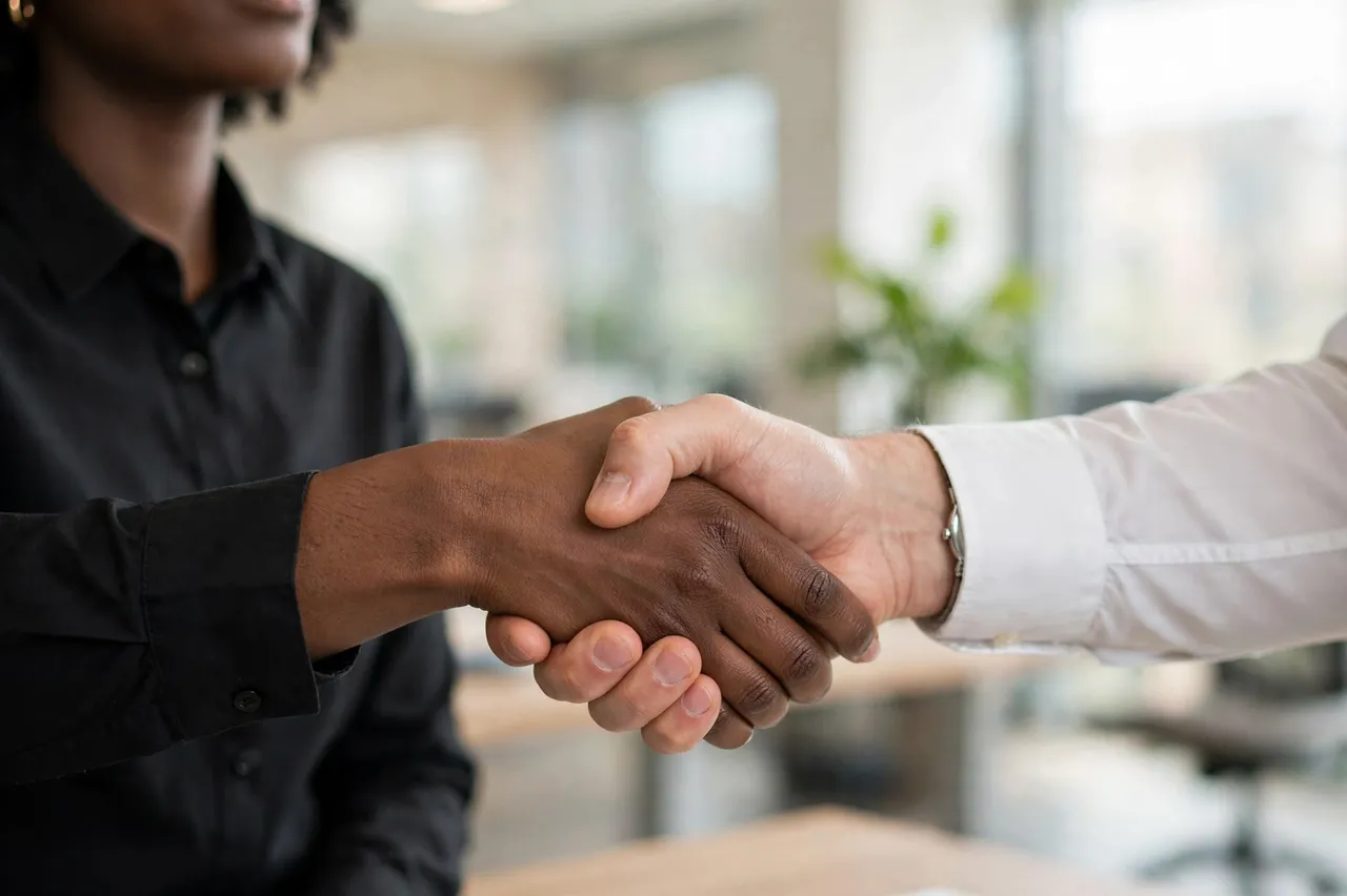 Close-up of a handshake between two people in business shirts inside a bright blurred office