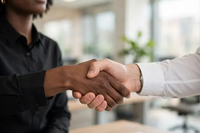 Close-up of a handshake between two people in business shirts inside a bright blurred office