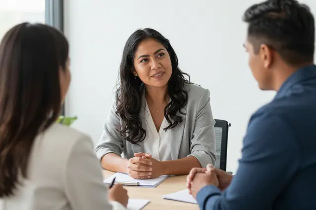 Three people sit across a light office table during a professional meeting or job interview