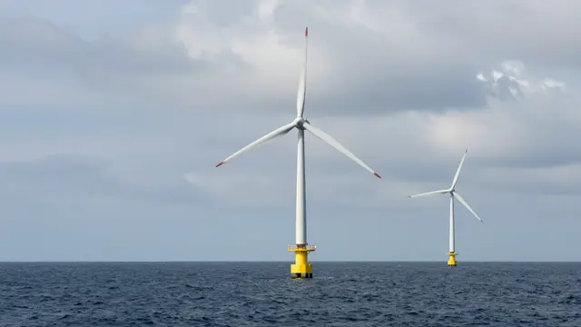 Two offshore wind turbines stand in dark ocean water beneath an overcast cloudy sky.