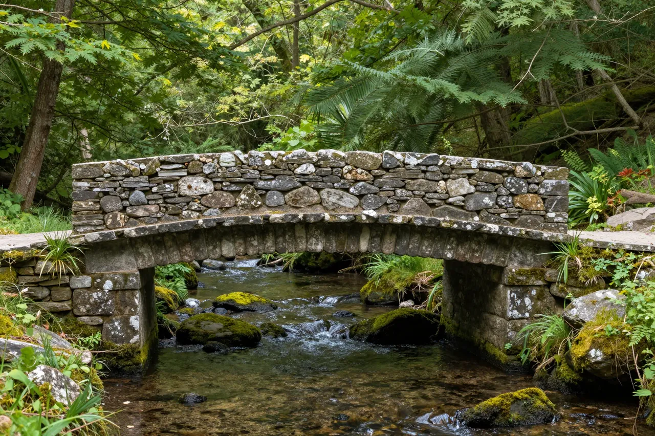 Weathered dry-stone footbridge spans a mossy shallow stream in a lush summer wooded ravine