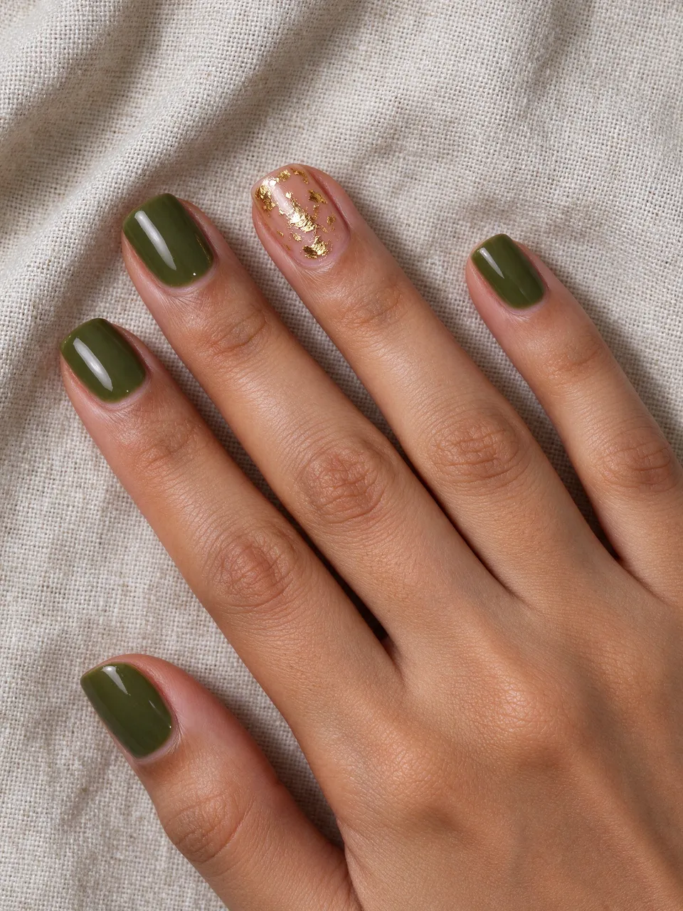 Close-up of a South Asian woman's hand with olive squoval nails and a gold foil accent resting on linen fabric